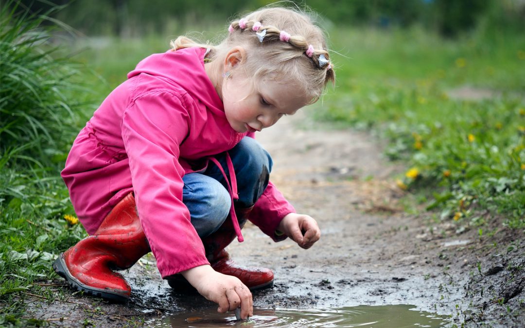 Urban Green Design Sensory Play The Importance of Risk in play Blog Featured Image young child welly boots and a jacket playing in a puddle outside